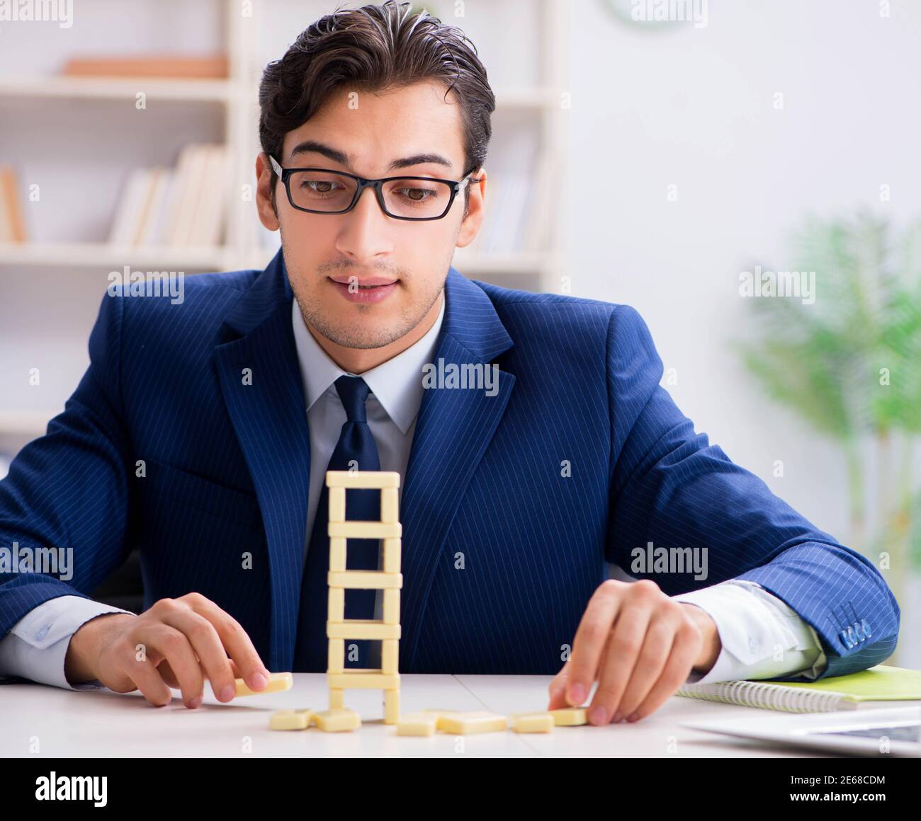 The young businessman building domino tower in office Stock Photo - Alamy