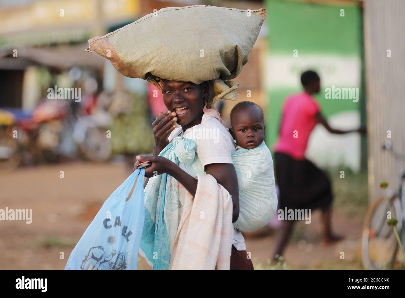 A woman carries a child and a bag on her head within the trading centre of the U.S. President Barack Obama's ancestral village of Nyang'oma Kogelo, west of Kenya's capital Nairobi, July 15, 2015. President Obama visits Kenya and Ethiopia in July, his third major trip to Sub-Saharan Africa after travelling to Ghana in 2009 and to Tanzania, Senegal and South Africa in 2011. He has also visited Egypt, in North Africa, and South Africa for Nelson Mandela's funeral. Obama will be welcomed by a continent that had expected closer attention from a man they claim as their son, a sentiment felt acutely  Stock Photo