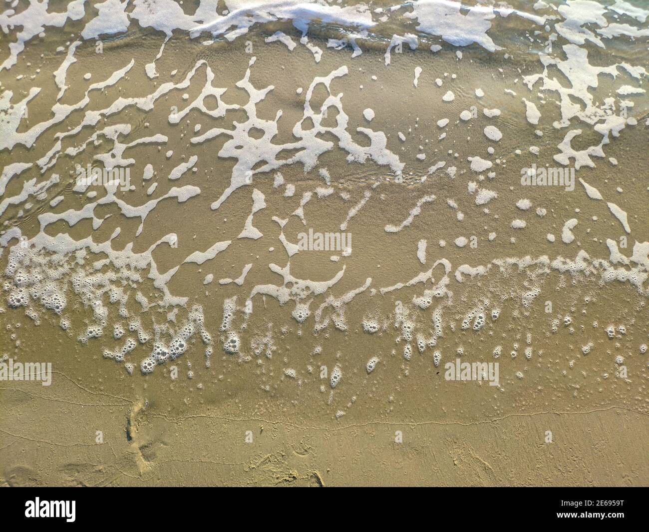 white foam runs with sea water on the yellow sand beach Stock Photo