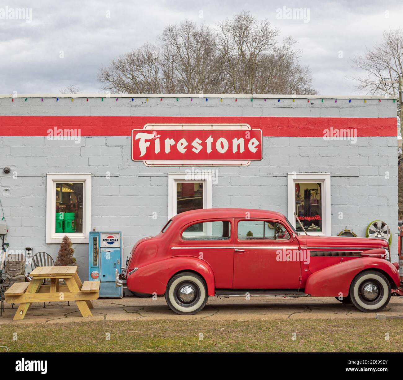 1940s car next to an old building with a firestone sign Stock Photo