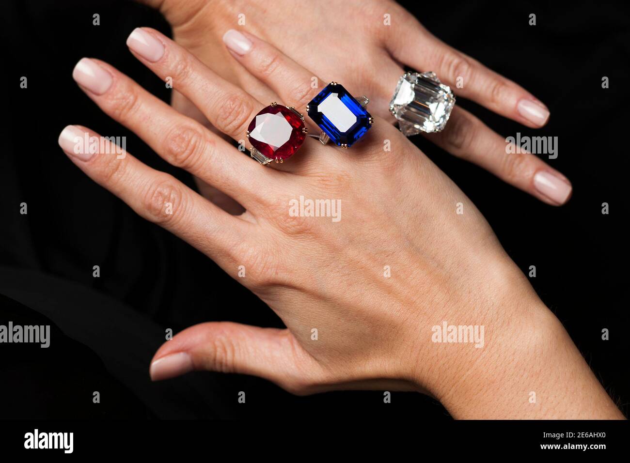A employee poses with a rectangular cut diamond ring, an oval shaped ruby  and diamond ring and a rectangular cut sapphire and diamond ring from the  Lily Safra collection during an auction