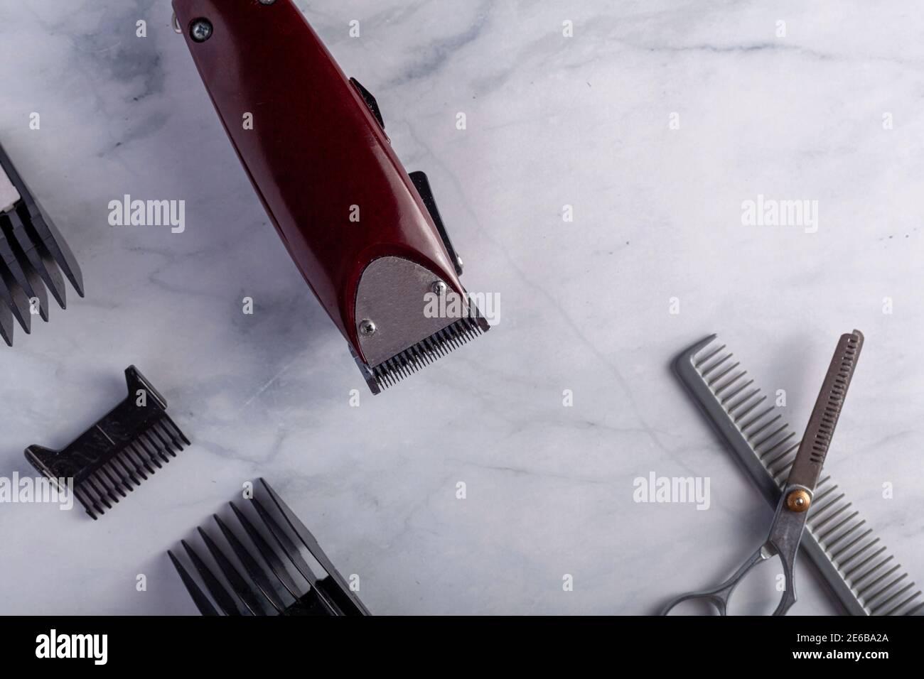 Flat lay close up image of a hair trimming kit featuring a corded electrical hair clipper with different sizes of comb guards, thinning shear type sci Stock Photo