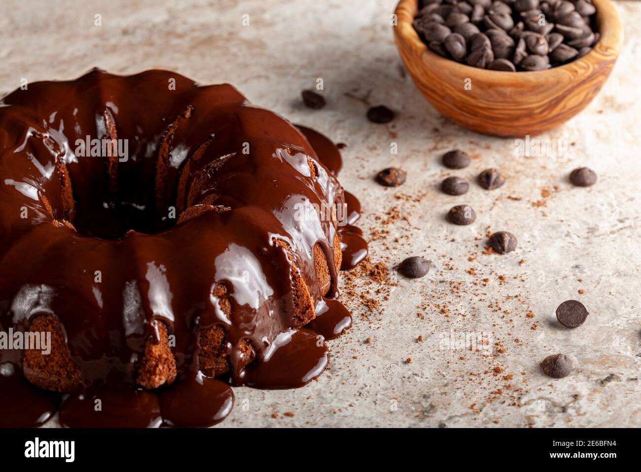 Angled view of a chocolate bundt cake with chocolate pudding icing dripping on top of it. There are cacao powder and chocolate chips on the surface wi Stock Photo