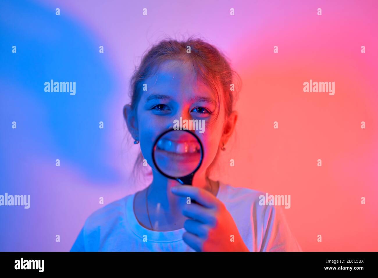 A nice little girl looks through a magnifying glass. The concept of a happy childhood, science and education of a child in the family. Isolated on whi Stock Photo