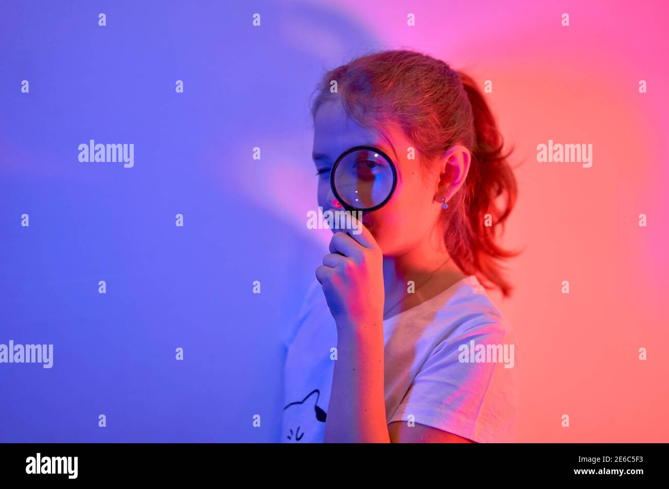 A nice little girl looks through a magnifying glass. The concept of a happy childhood, science and education of a child in the family. Isolated on whi Stock Photo