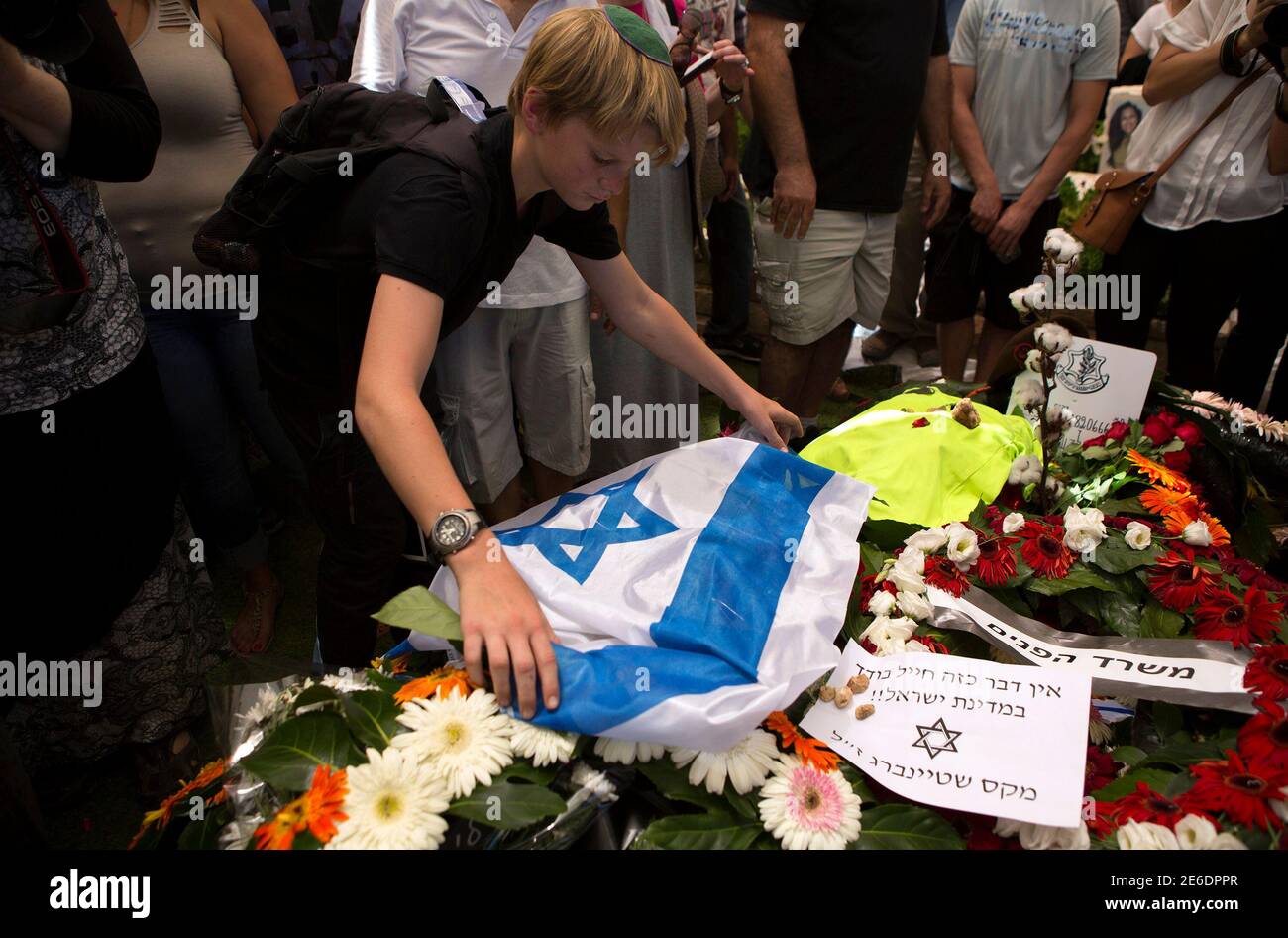 A mourner places an Israeli flag on the grave of fallen soldier Max Steinberg during his funeral at Mount Herzl military cemetery in Jerusalem July 23, 2014. Steinberg, a 23 year-old American from California's San Fernando Valley, was among 13 Israeli Defense Forces soldiers killed on Sunday during fighting in Gaza. REUTERS/Siegfried Modola (JERUSALEM - Tags: CONFLICT POLITICS CIVIL UNREST MILITARY) Stock Photo