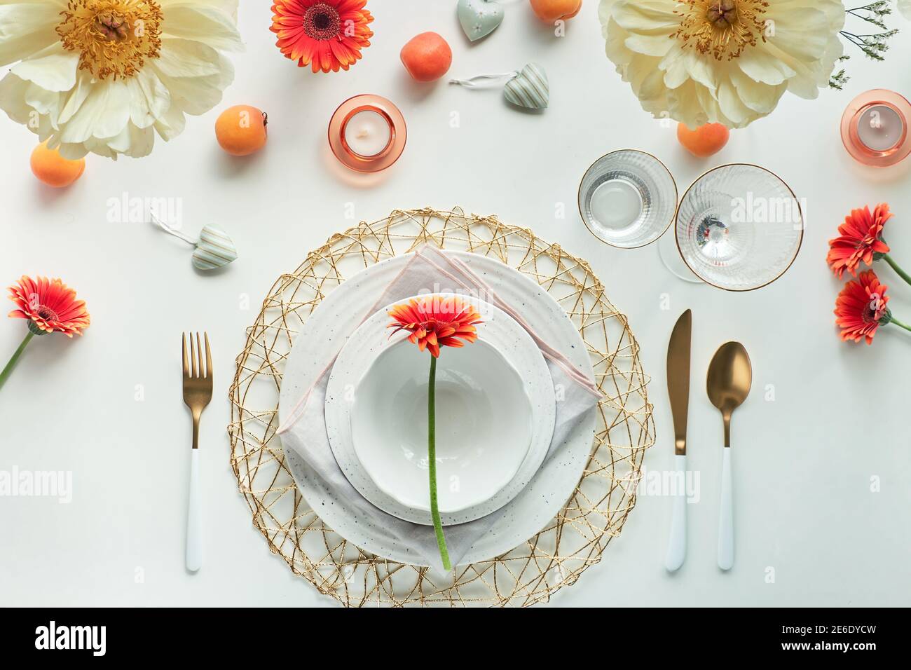 Effortless golden birthday dinner table decor. Summer flat lay. White dinner table, white and gold utensils, decorated with peony flowers, orange Stock Photo