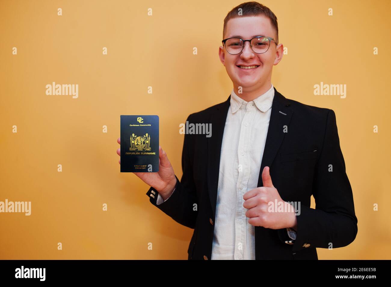 Young handsome man holding Republic of Suriname passport id over yellow background, happy and show thumb up. Travel to America countries. Stock Photo