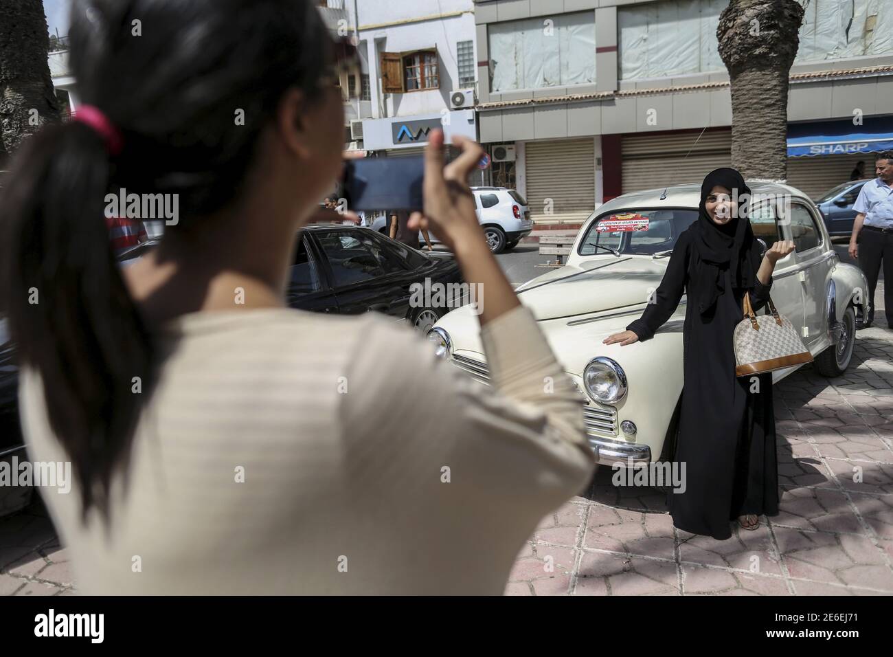 A woman photographs her friend during a vintage car exhibition in Rouiba, on the outskirt of Algiers, Algeria June 12, 2015. The local Algerian association “Nass Al Kheir” organized a vintage car exhibition in Algiers to raise awareness of road accident prevention. Association president Samir Kafia Said  said that the show was aimed at teaching people about keeping to speeds under 100. According to the Directorate General for National Security (DGSN) Algeria is in top ten nations in numbers of cars accident fatalities with 4000 death per year. REUTERS/Zohra Bensemra Stock Photo