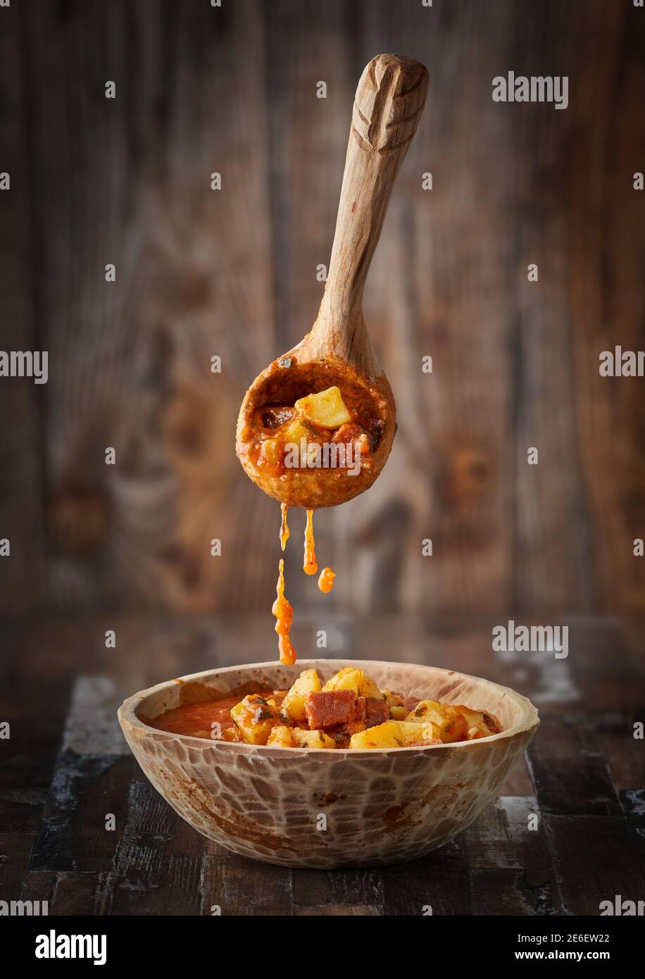 Flying food - levitating wooden ladle pouring potato stew with pork in a  rustic bowl Stock Photo - Alamy