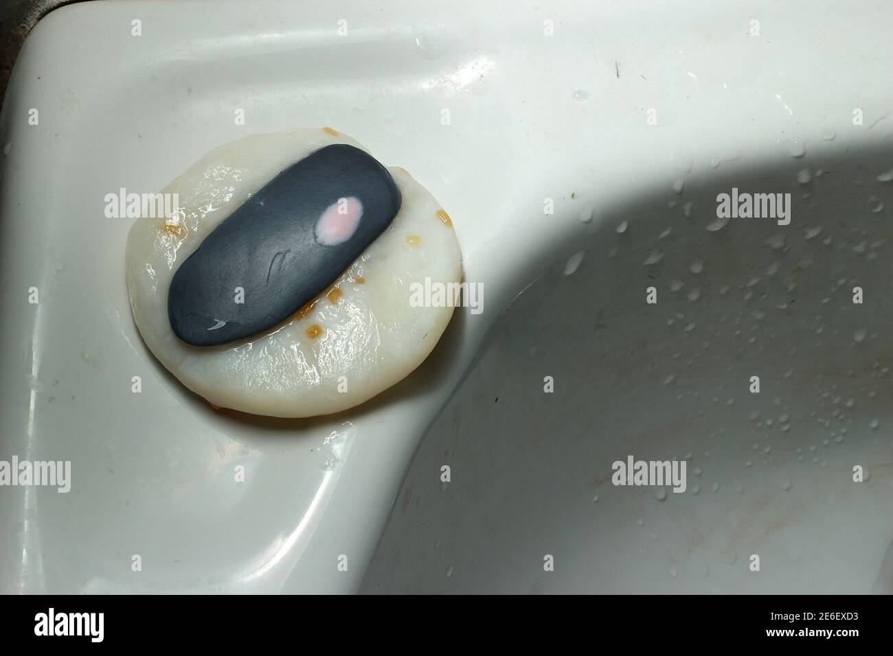 The pink soap is stuck on top of the black soap and the black soap is placed on top of the white soap. This soap is placed by the sink. Stock Photo