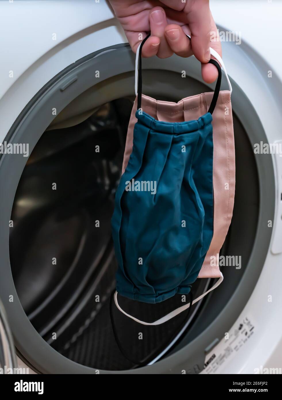 Hand putting used cloth face masks into a washing machine Stock Photo