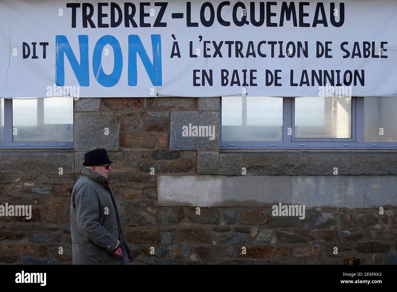 A man walks in front of a banner which reads: "Tredrez-Locquemeau say No to the extraction of sand in the bay of Lannion" in Tredrez-Locquemeau, December 17, 2016. REUTERS/Stephane Mahe Stock Photo