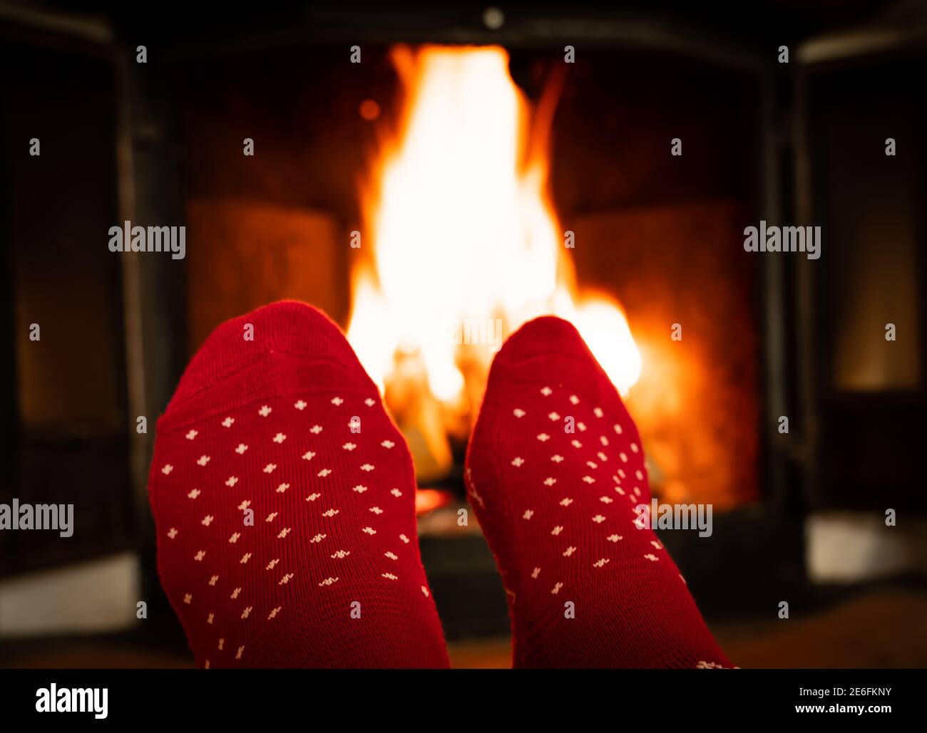 Female feet in red woolen socks by a warm fireplace on a cold winters evening. Stock Photo