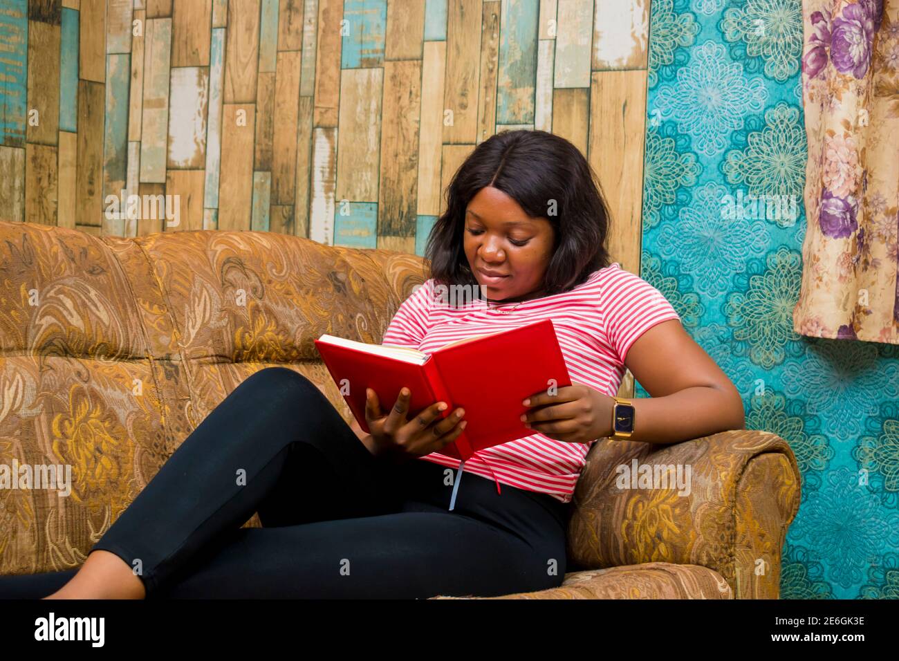 young black lady sitting on a couch, listening to songs on her phone, studying, writing and surfing the internet Stock Photo