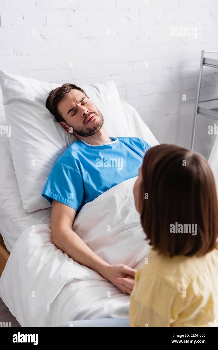 girl holding hand of sick father frowning while lying with hospital bed with closed eyes Stock Photo