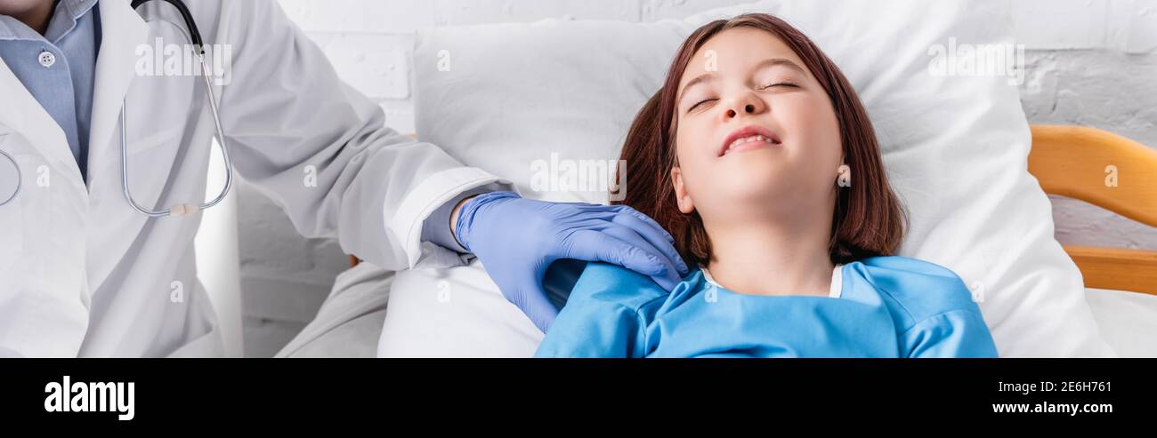 pediatrician examining sick girl lying in bed with closed eyes, banner Stock Photo
