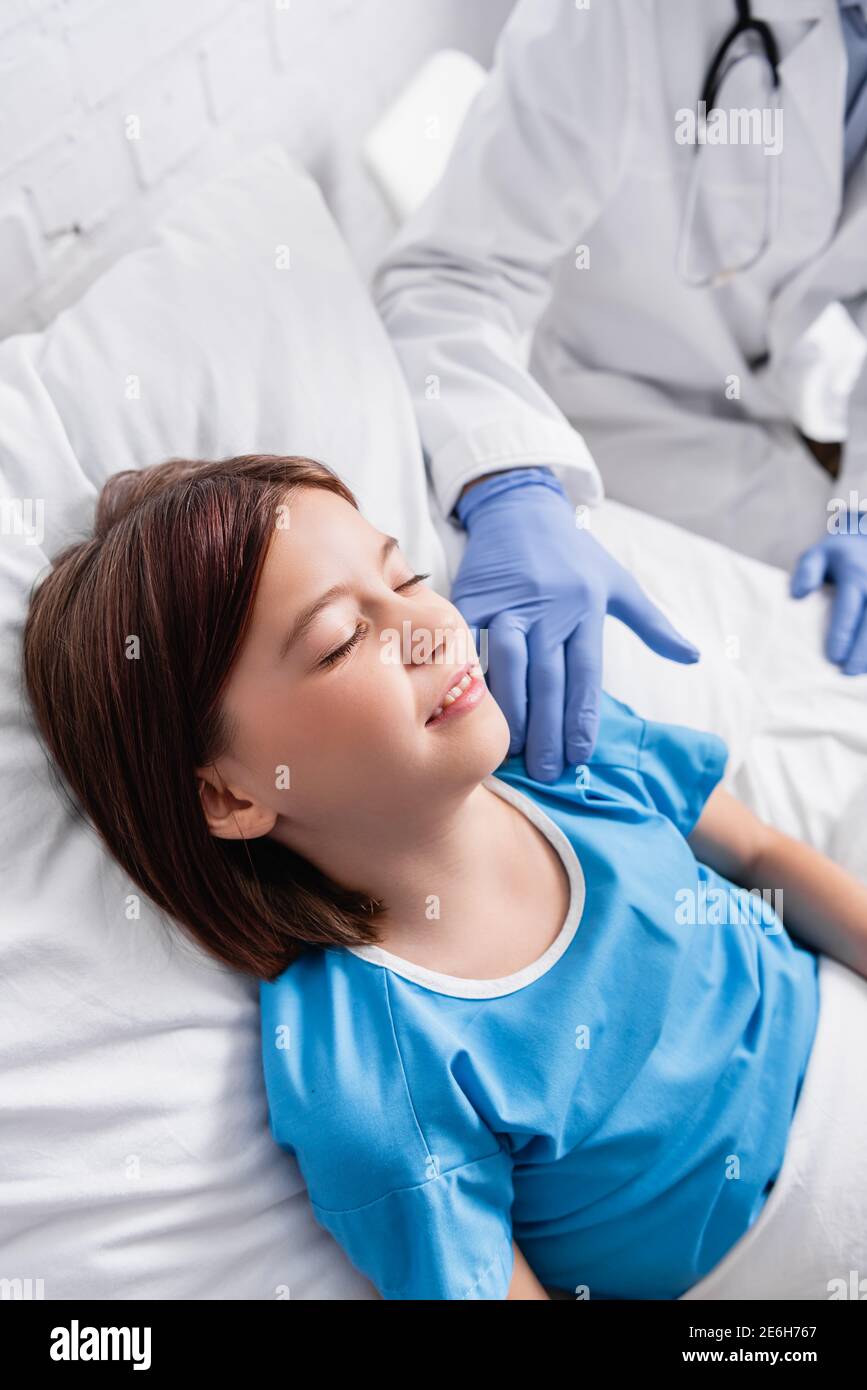 doctor touching child lying in hospital bed with closed eyes, blurred background Stock Photo