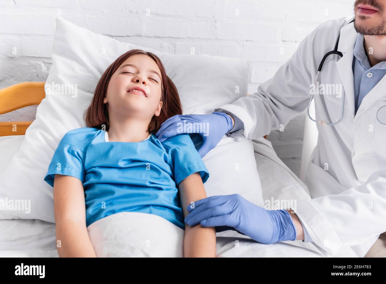 pediatrician examining diseased girl lying in bed with closed eyes Stock Photo