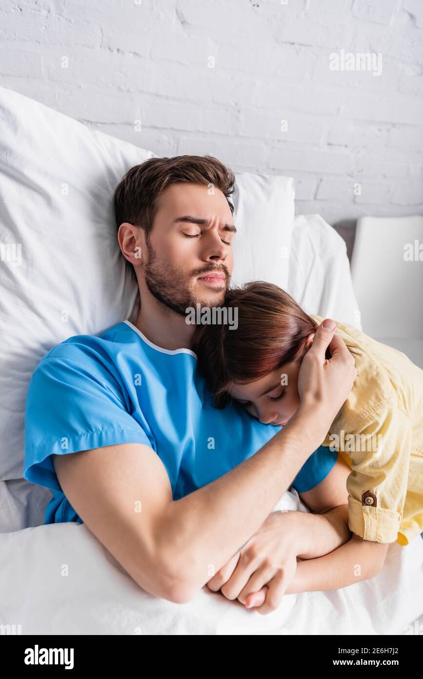 sick man embracing daughter while lying in hospital bed with closed eyes Stock Photo
