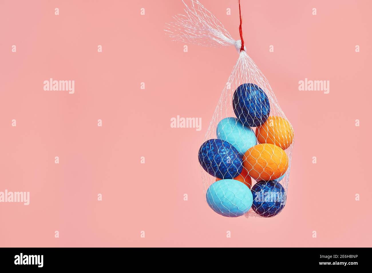 multi-colored chicken eggs in  bag mesh hang on pink background. easter Stock Photo