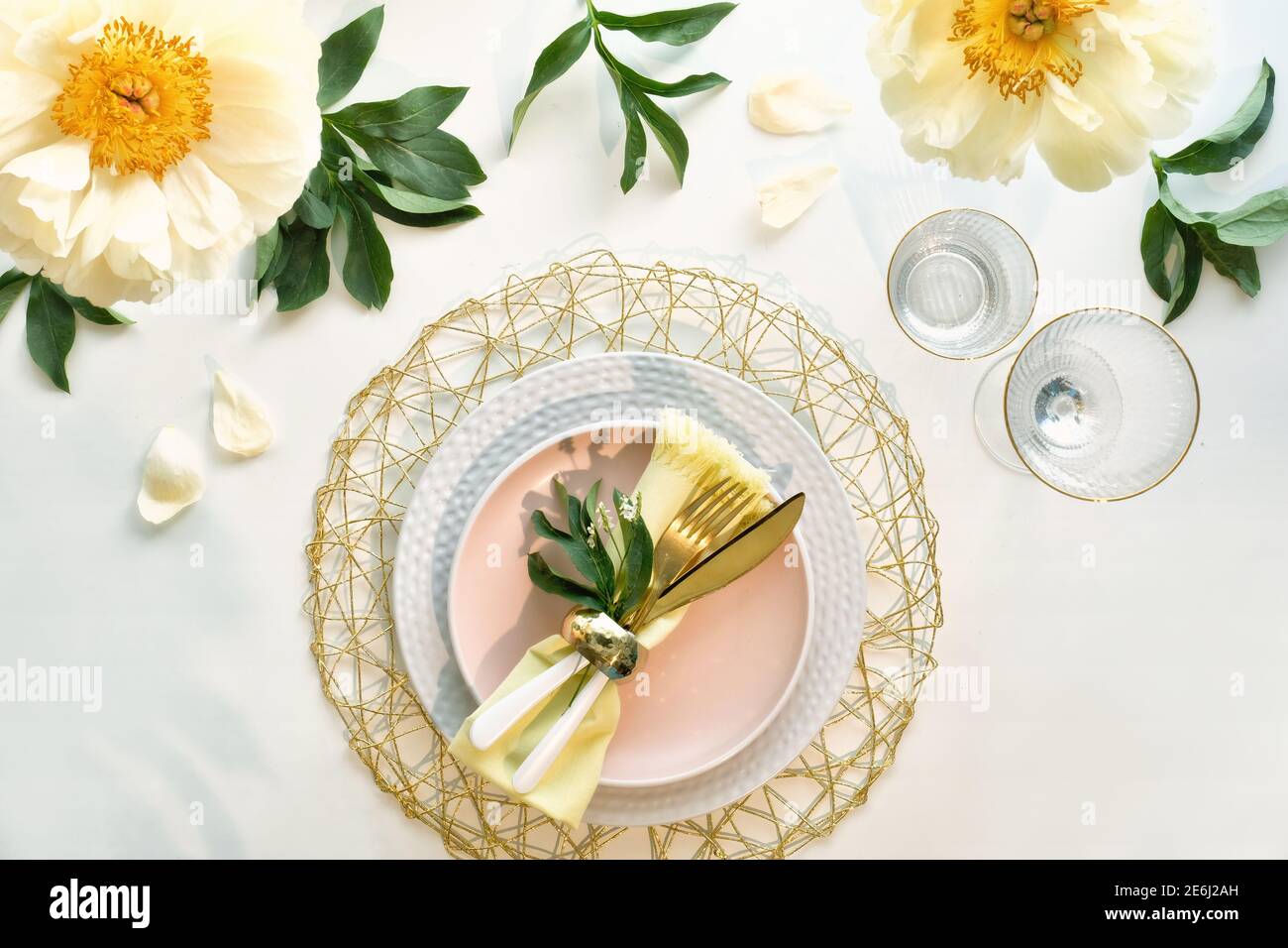 Effortless golden birthday dinner table decor. Pale yellow peony flowers and Late Spring, Summer flat lay. White dinner table, white, gold utensils Stock Photo