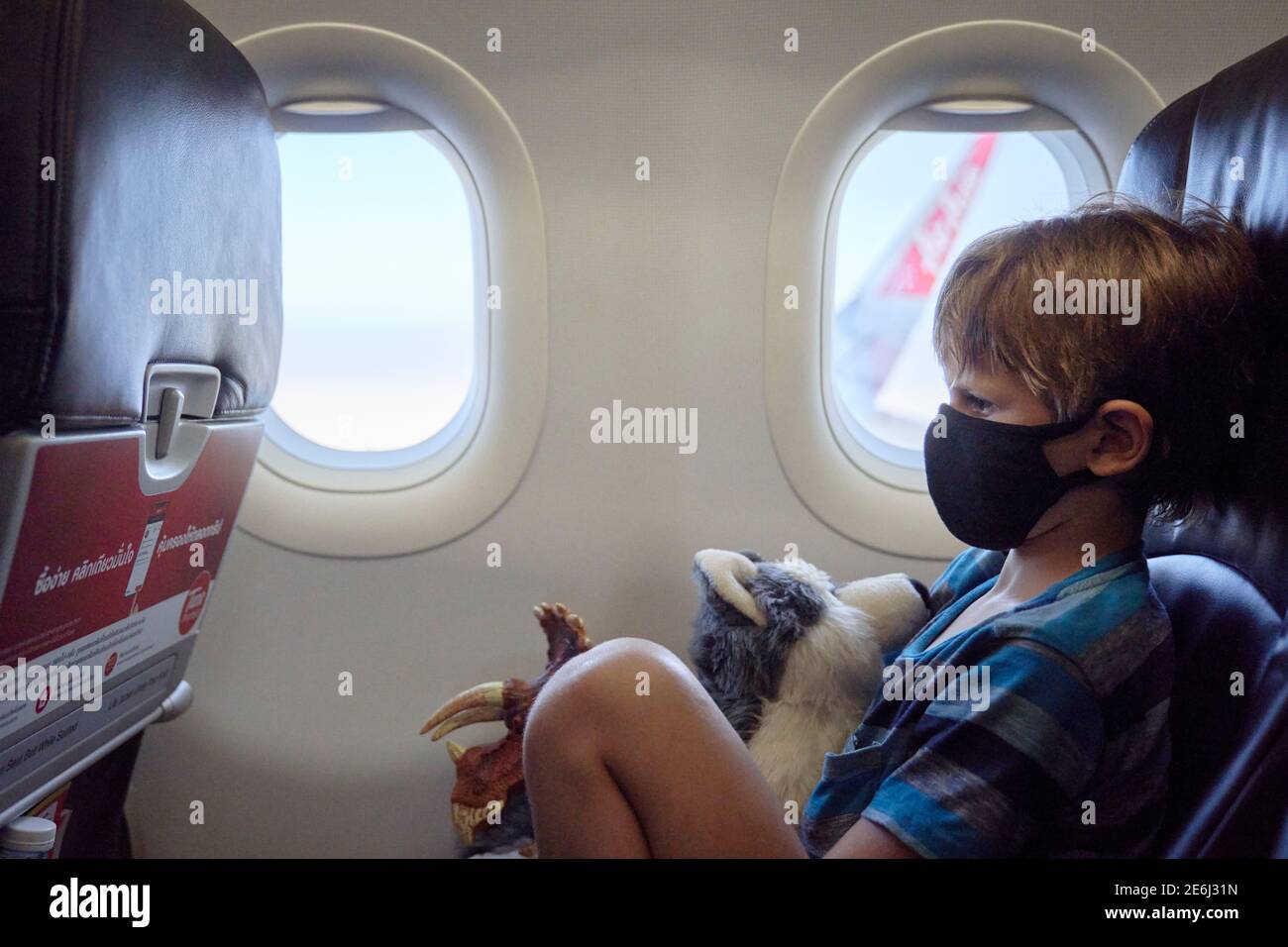 A child on an airplane holding a soft toy and wearing a face mask Stock