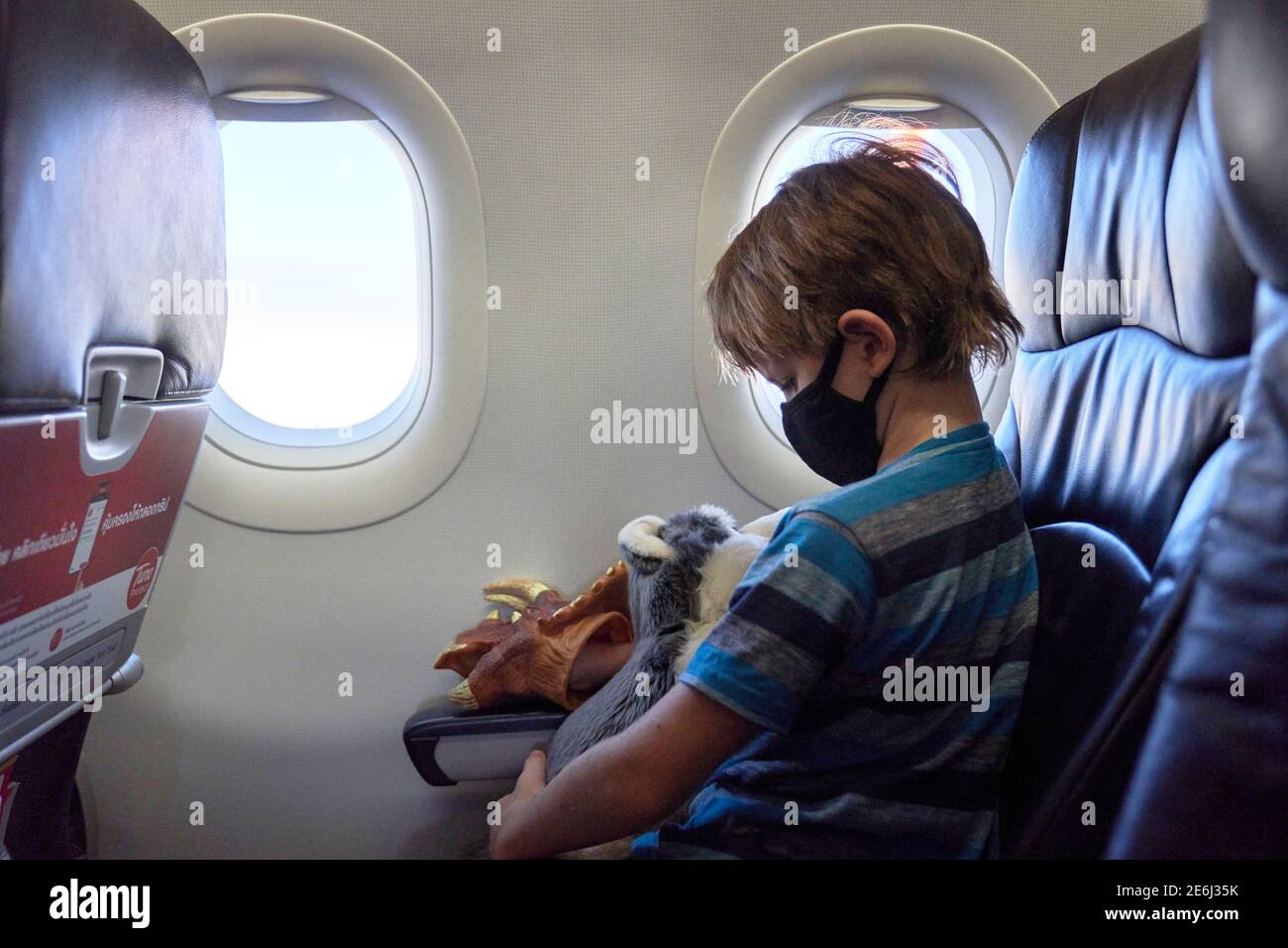 A child on an airplane holding a soft toy and wearing a face mask Stock