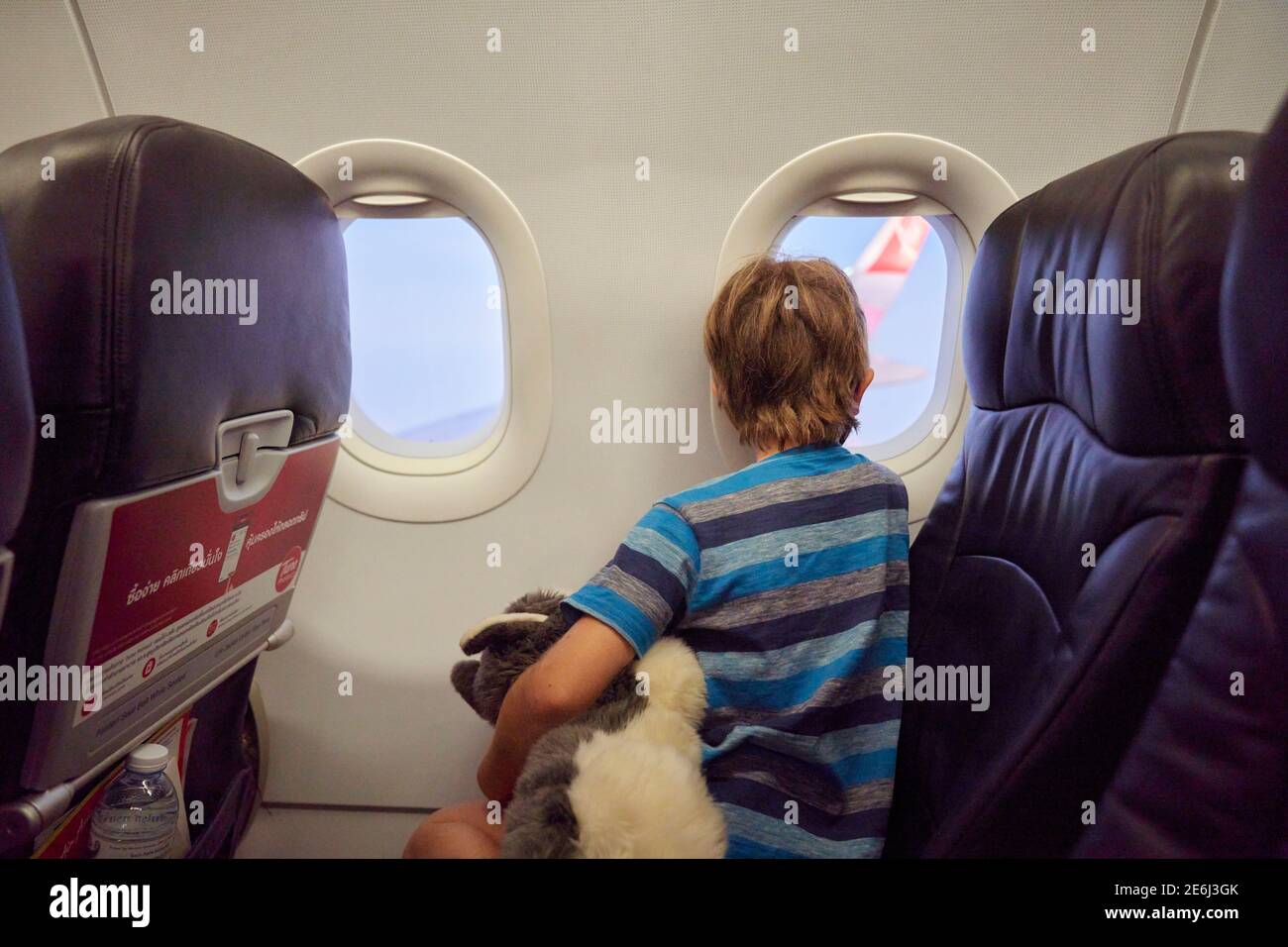 A child on an airplane holding a soft toy and wearing a face mask