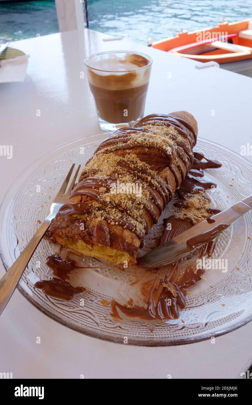 A chocolate croissant and coffee served at a greek waterside bar Stock