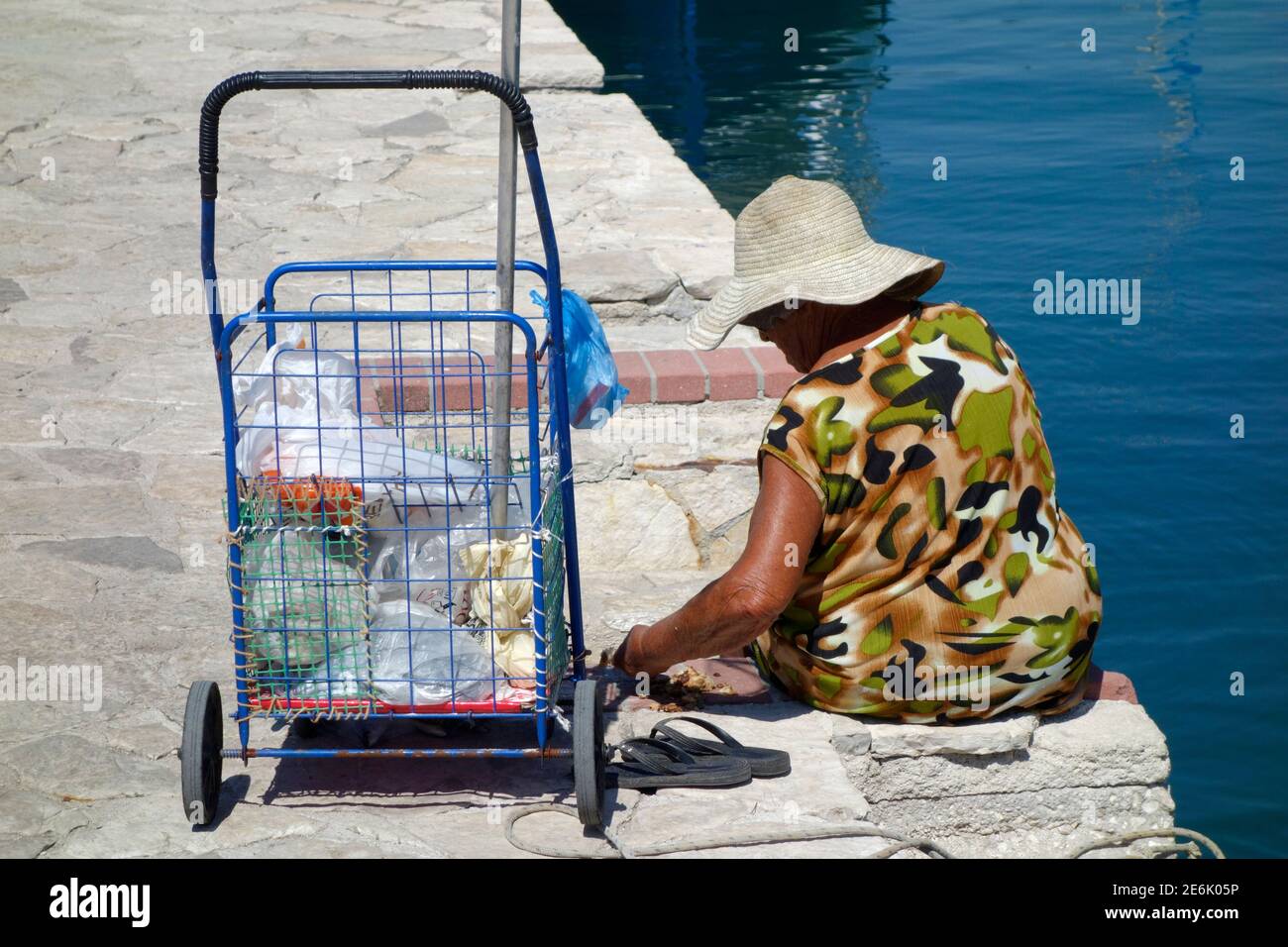 Elderly greek woman with a shopping trolly sitting on the quayside in Vathy, Ithaca Stock Photo