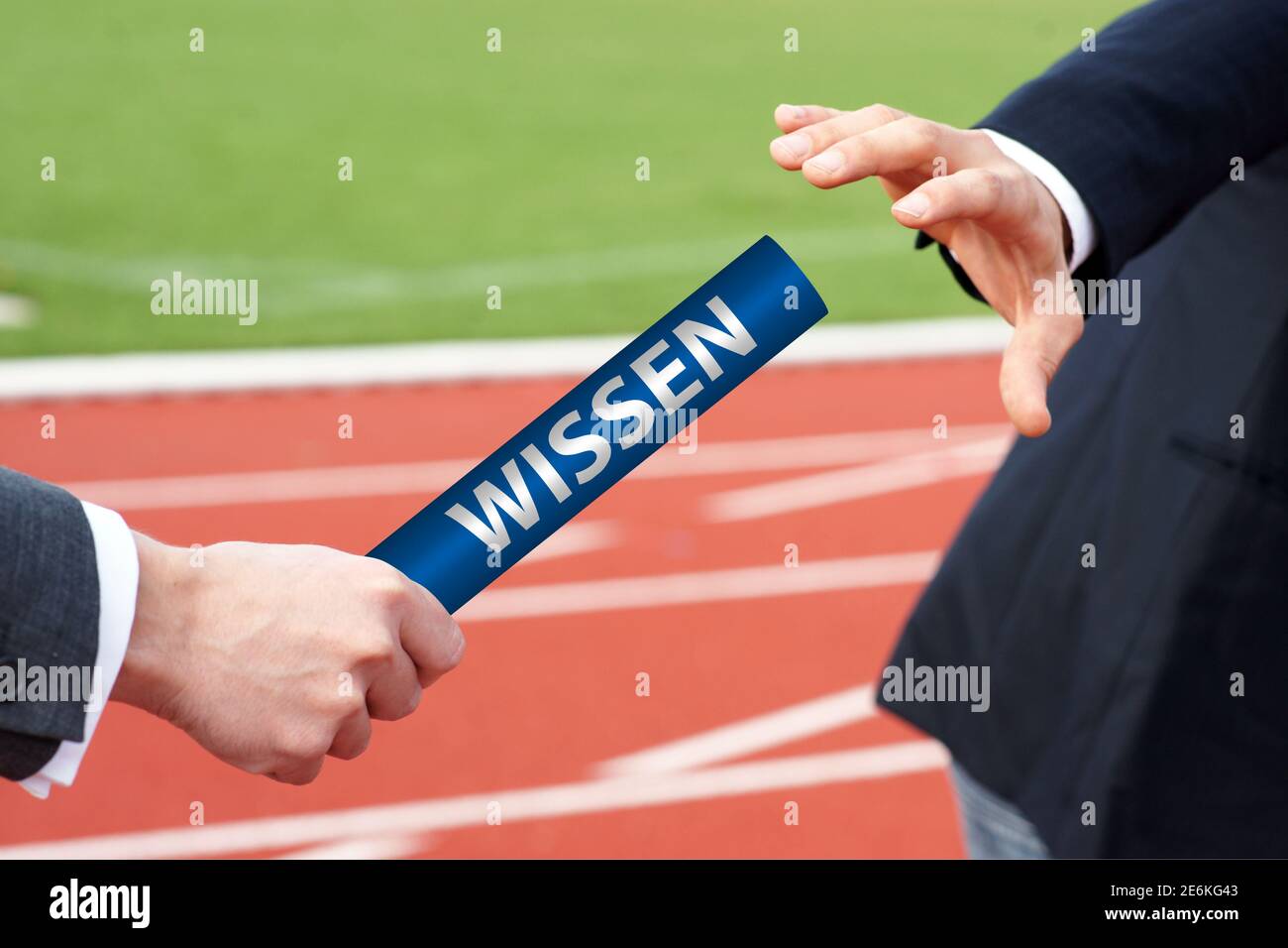 Businessmen passing baton in relay race with German word Wissen means Knowledge  Stock Photo