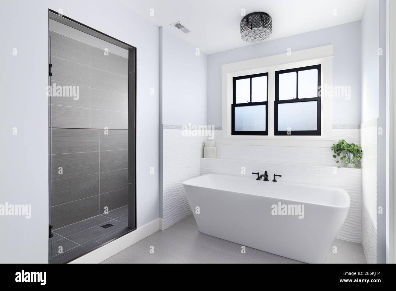 A beautiful, luxury bathroom with a light hanging above a white Fleurco standalone tub and black faucet surrounded by tiles and a marble tiled shower. Stock Photo