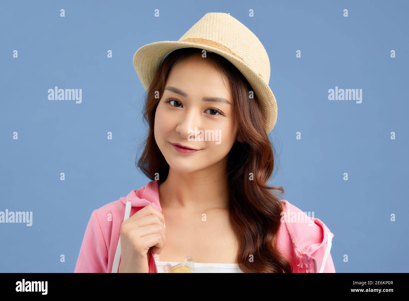 Portrait of young Asian woman wearing hat, t-shirt, short jeans and pink jacket isolated over blue background. Stock Photo