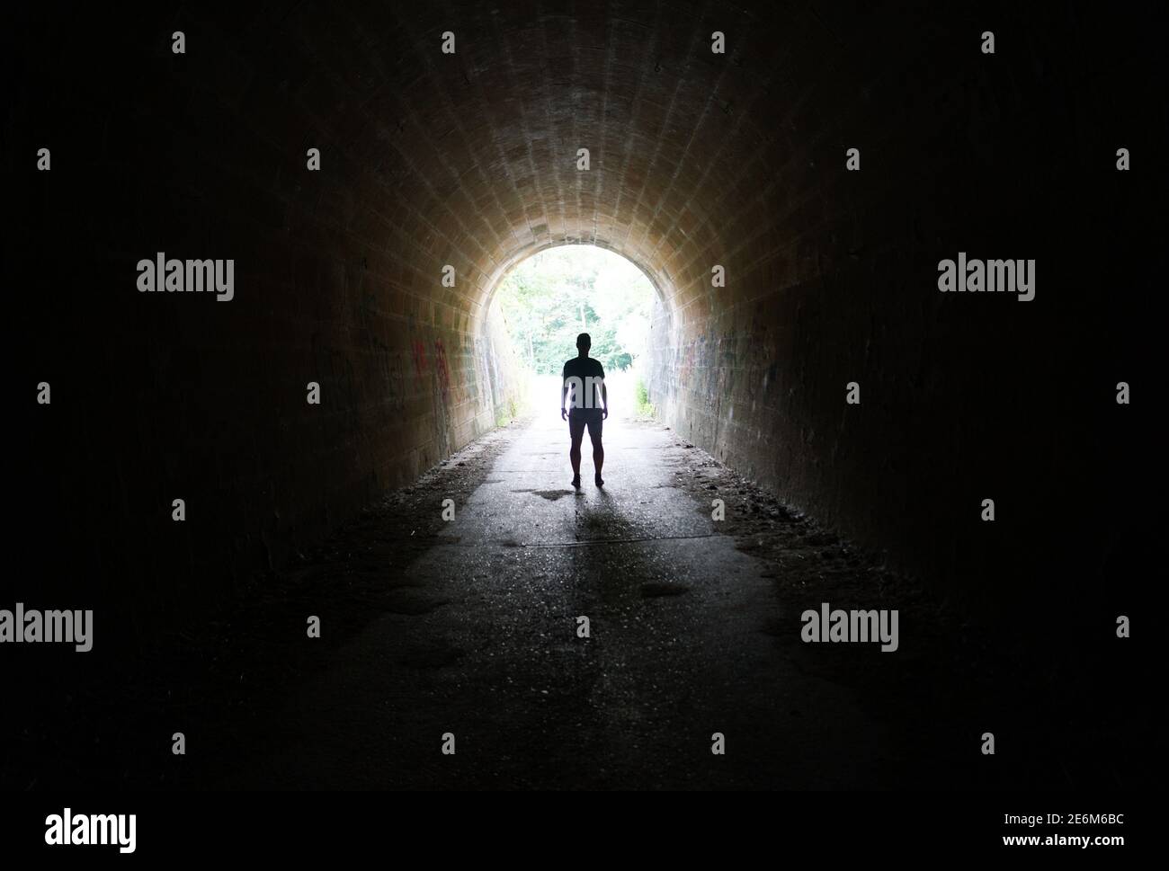 Escape the Darkness - silhouette of man standing in the light at the end of the tunnel Stock Photo