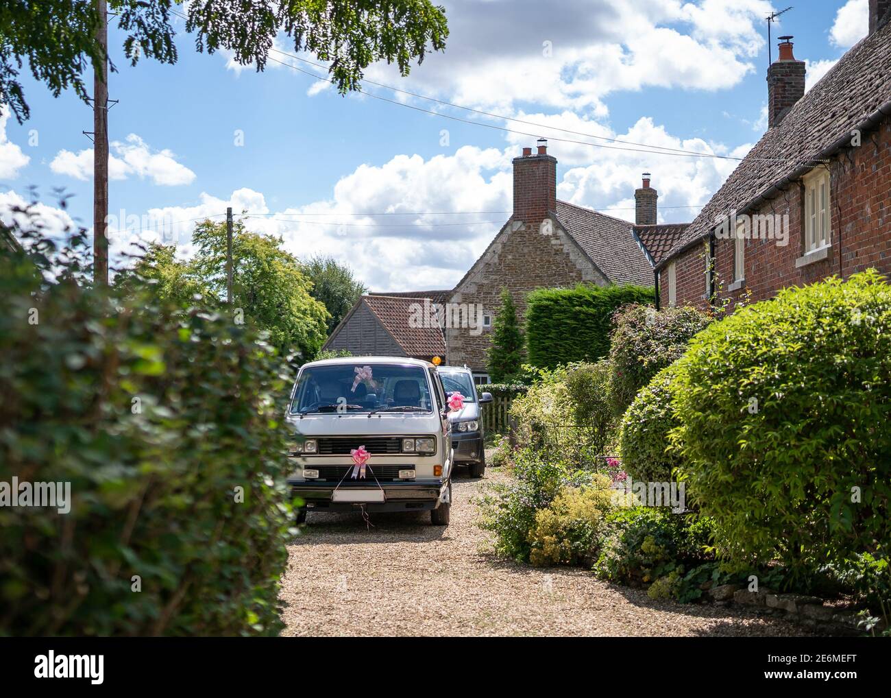 Wedding beautiful polished clean classic camper van with pink ribbons parked on driveway outside a countryside cottage in sunshine waiting for bride Stock Photo