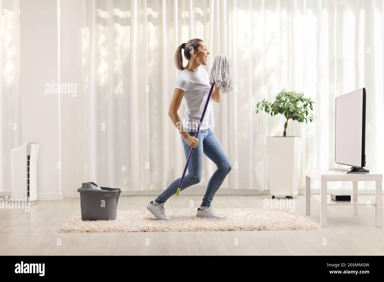 Happy young woman dancing and singing with a cleaning mop in front of ...