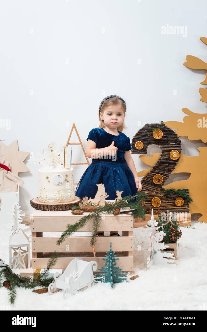 Children's winter birthday decorations. Cute little girl in a dark blue  dress near white birthday cake Stock Photo - Alamy