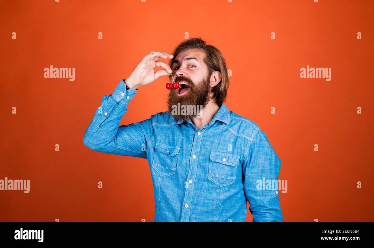 just one bite. confident farmer with fresh fruits. bearded man holding ripe cherries. Harvesting in summer. happy mature hipster with beard. brutal caucasian guy with cherry. organic fruits. Stock Photo