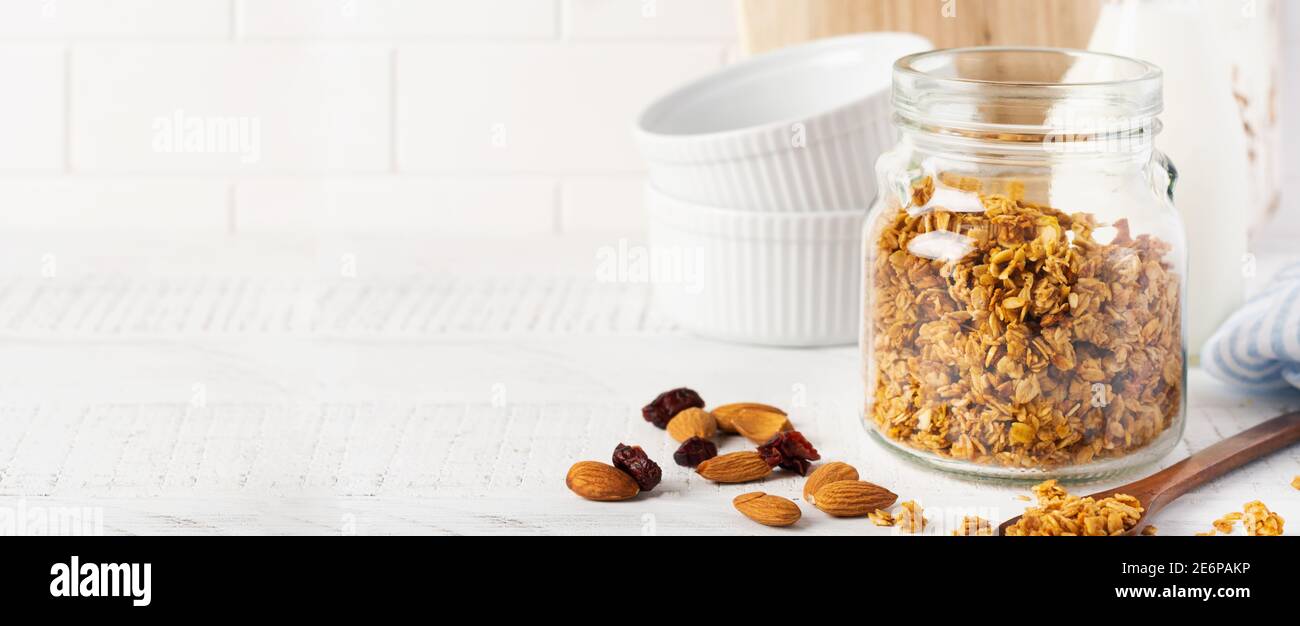 Oat granola with a bottle of milk, nuts and dried fruits, ceramic bowls for preparing a healthy breakfast on a bright kitchen table. Scandinavian whit Stock Photo