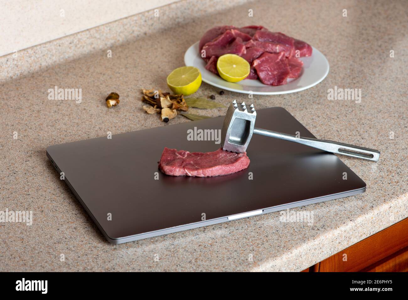 Computer is used as a kitchen board. Meat on laptop is ready to beat with tenderizer. Computer hating or testing. Stock Photo