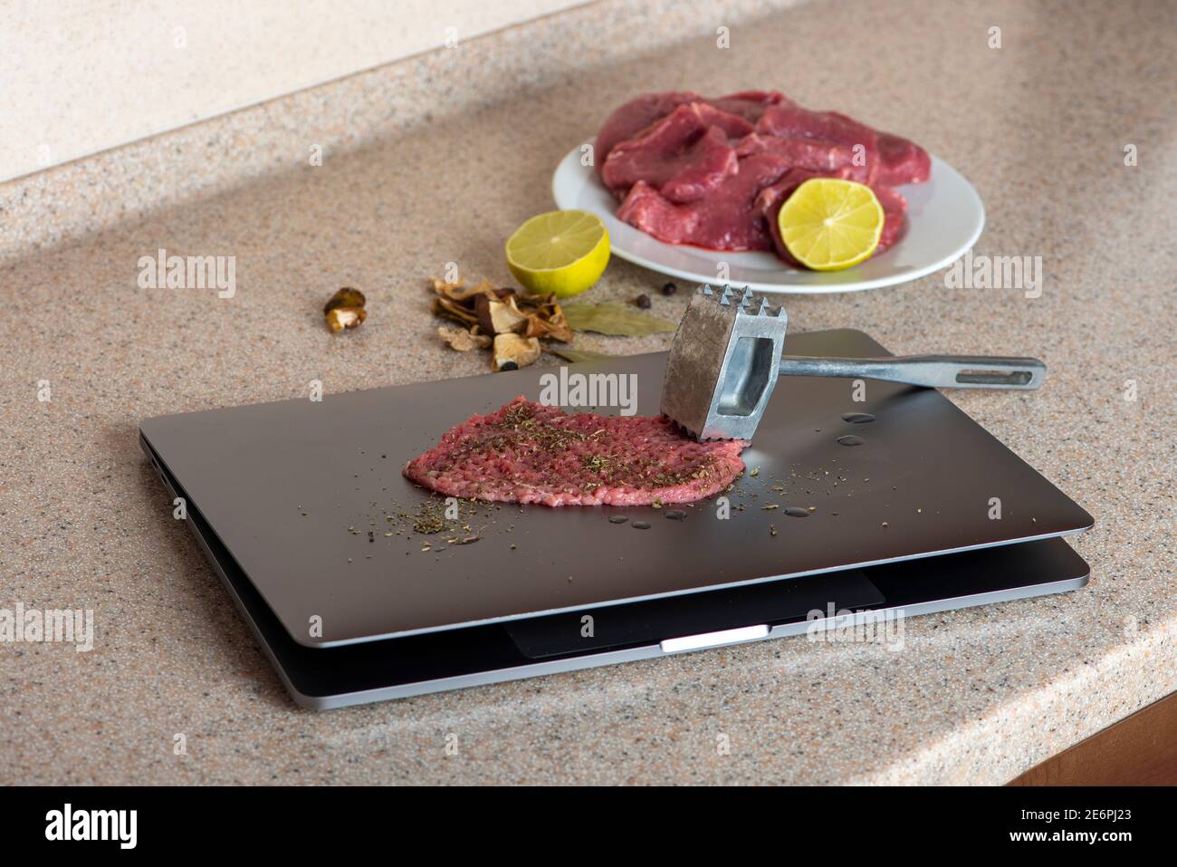 Computer is used as a kitchen board. Meat on laptop is ready to beat with tenderizer. Computer hating or testing. Stock Photo