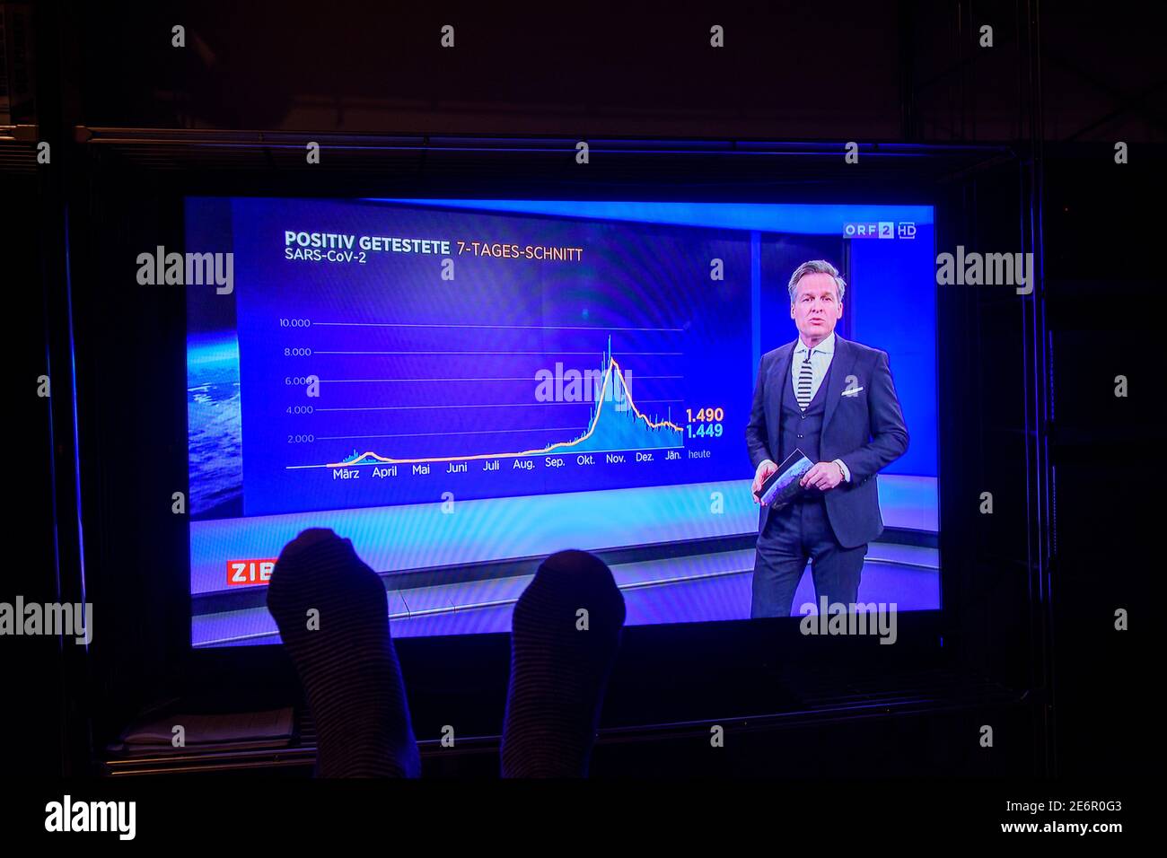 : TV set, Austrian television ORF, presenter Tarek Leitner shows covid-19 graphics in news program ZIB 1, feet of TV viewer sitting conveniently in fr Stock Photo