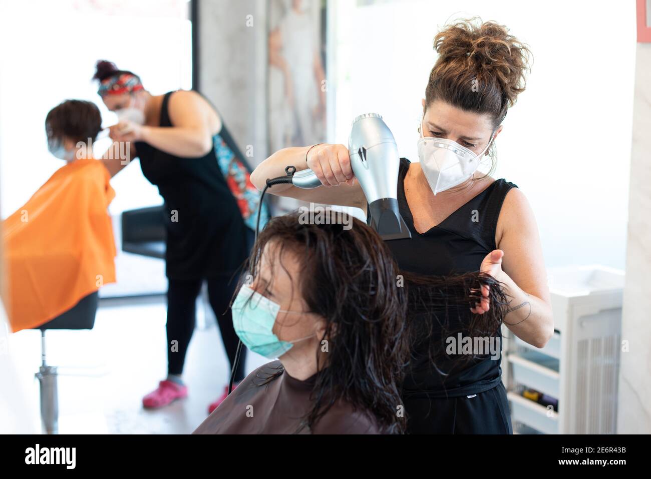 Working during covid-19 or coronavirus concept. A professional hairstylist cutting the hair to a client with a face mask. Stock Photo