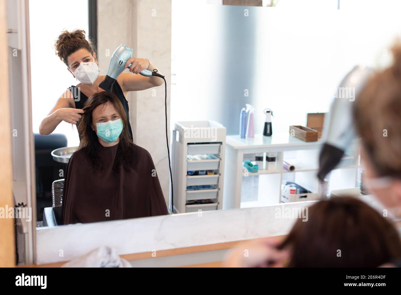 Working during covid-19 or coronavirus concept. A professional hairdresser cutting the hair to a client, reflected in the mirror with copy space. Stock Photo