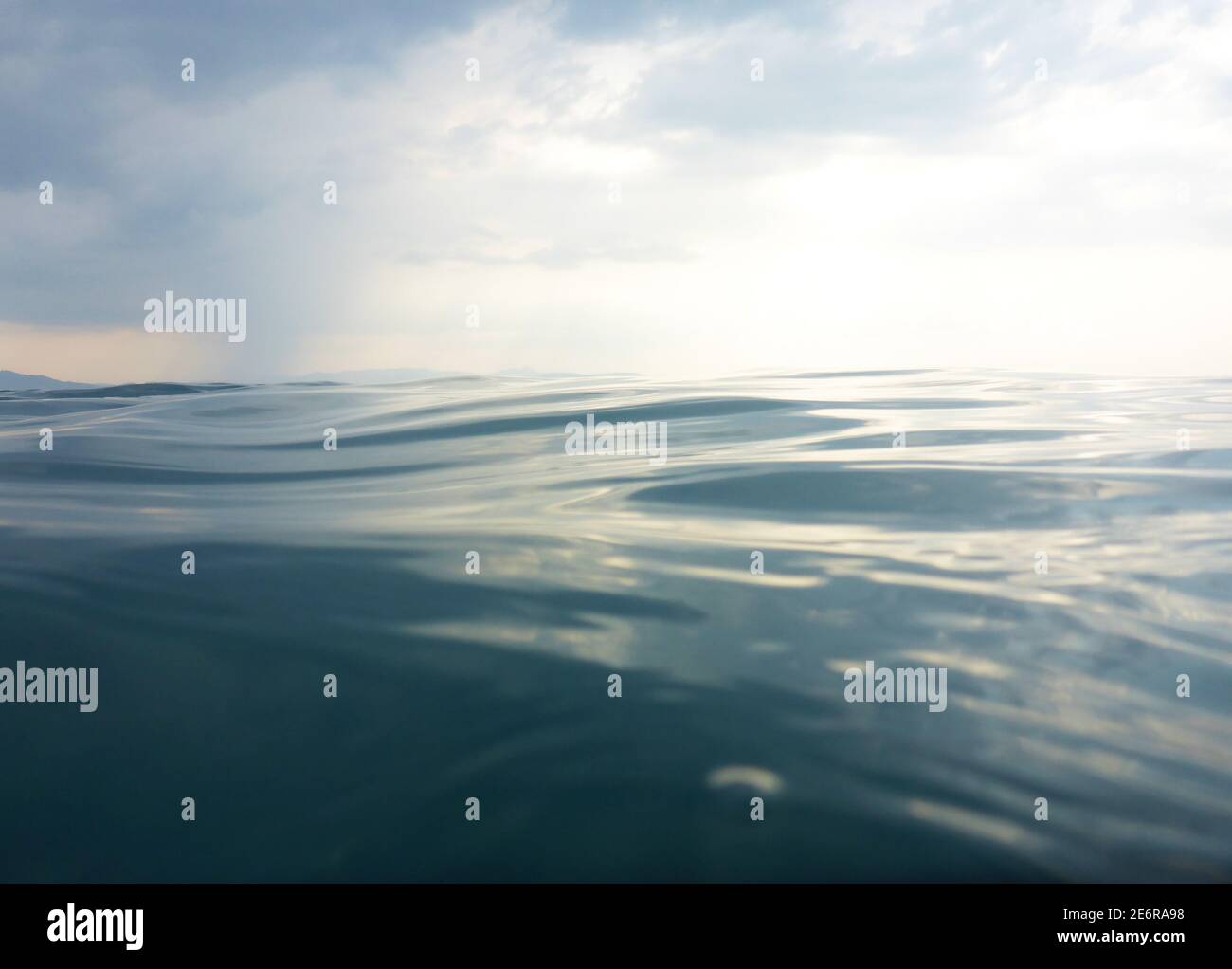 Background texture of clear, blue sea at water level and a cloudy evening sky Stock Photo