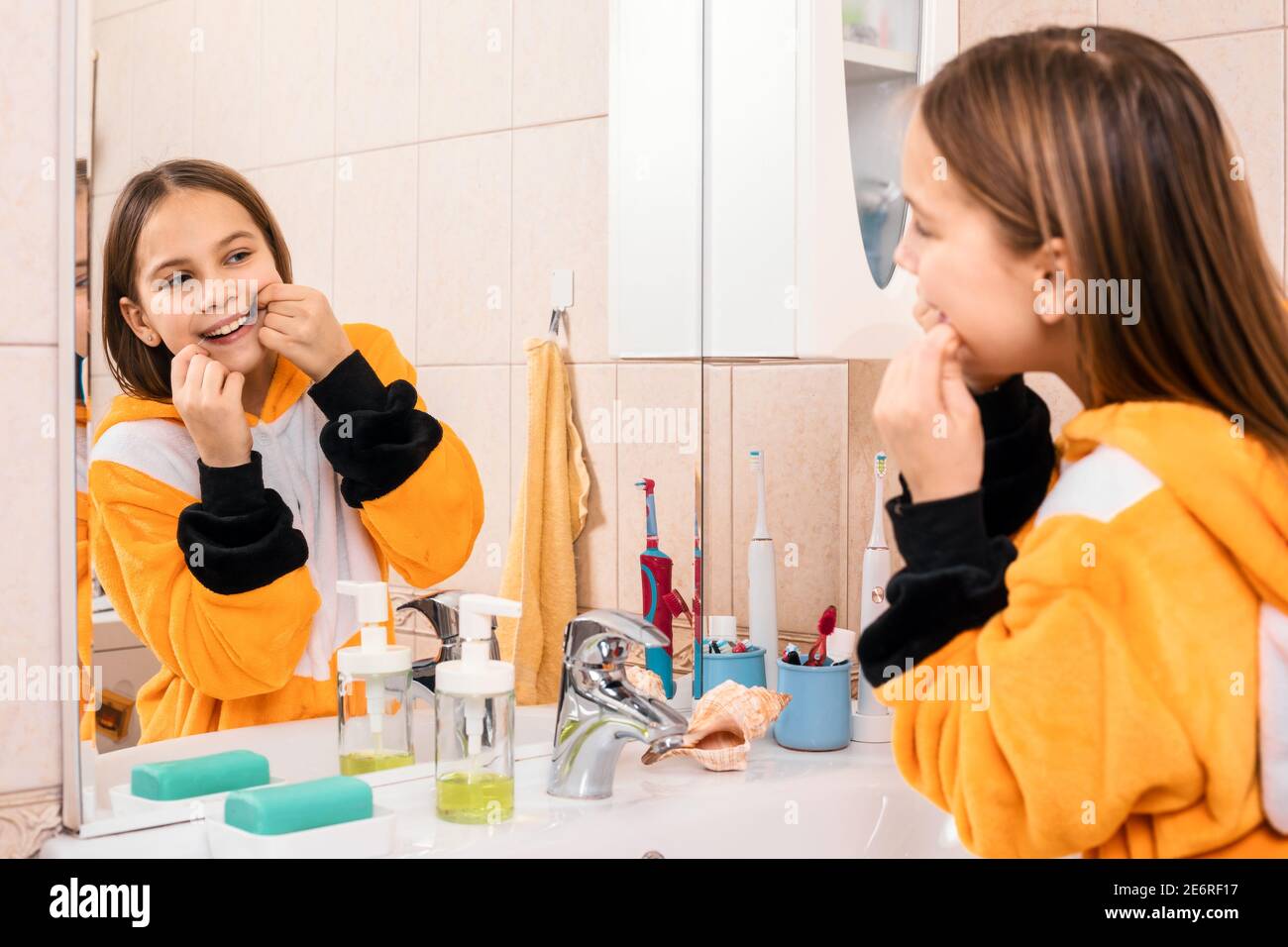 Tween girl wearing orange pyjamas uses dental floss to remove plaque between teeth Stock Photo