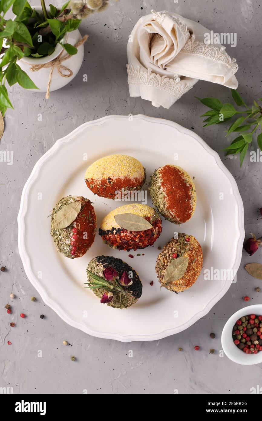 Easter eggs decorated with different spices and cereals without dyes and preservatives on a plate on a gray concrete background. Top view. Vertical fo Stock Photo