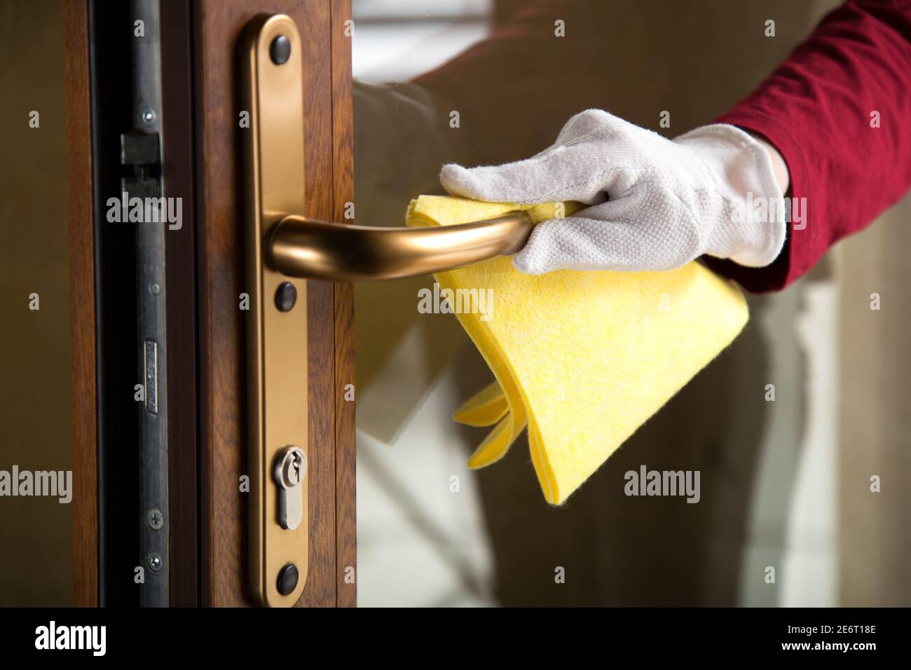 Woman clean entrance door handle doorknob with cloth. Hand in glove disinfecting surfaces by rag. The new normal Covid coronavirus in cleaning Stock Photo