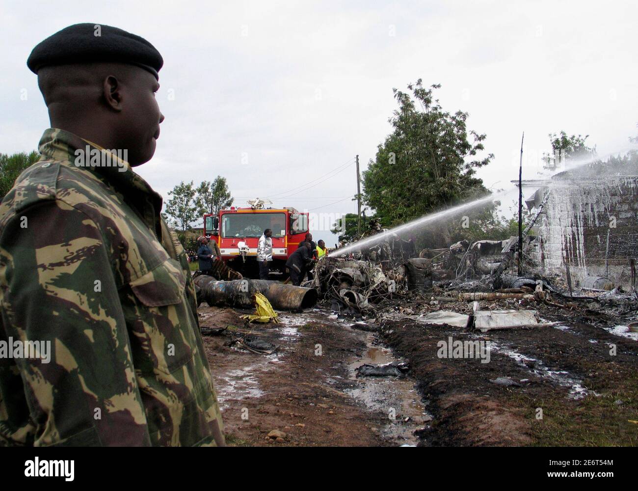 A policeman watches emergency workers put out a fire from the wreckage of a twin-engine Buffalo plane that crashed in Ruai, the outskirts of Kenya's capital Nairobi, December 30, 2006. A Kenyan plane carrying relief supplies and fuel to neighbouring war-torn Somalia crashed and burst into flames on Saturday, but officials said there were no fatalities. REUTERS/Thomas Mukoya (KENYA) Stock Photo